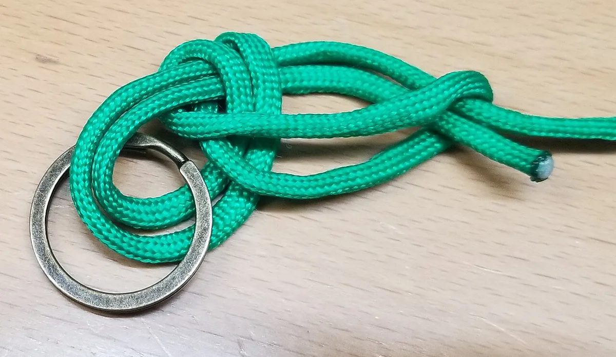 A argola já passou pela laçada; falta molhar e apertar (demonstração com cordão).