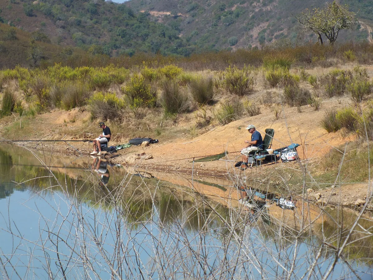 Pescadores sentados à beira da albufeira do Funcho, à espera do toque